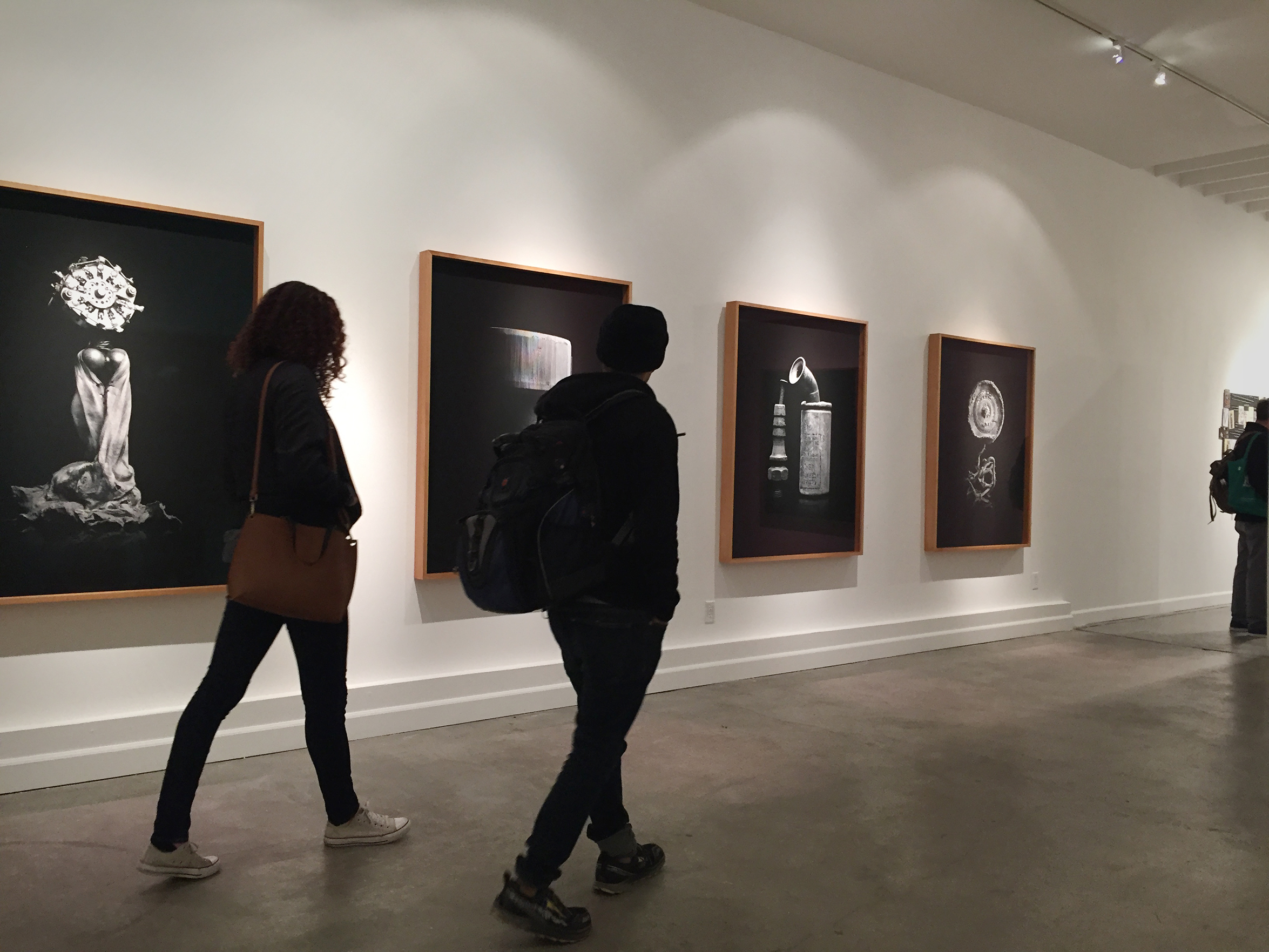 two figures walk in front of a series of black and white paintings.