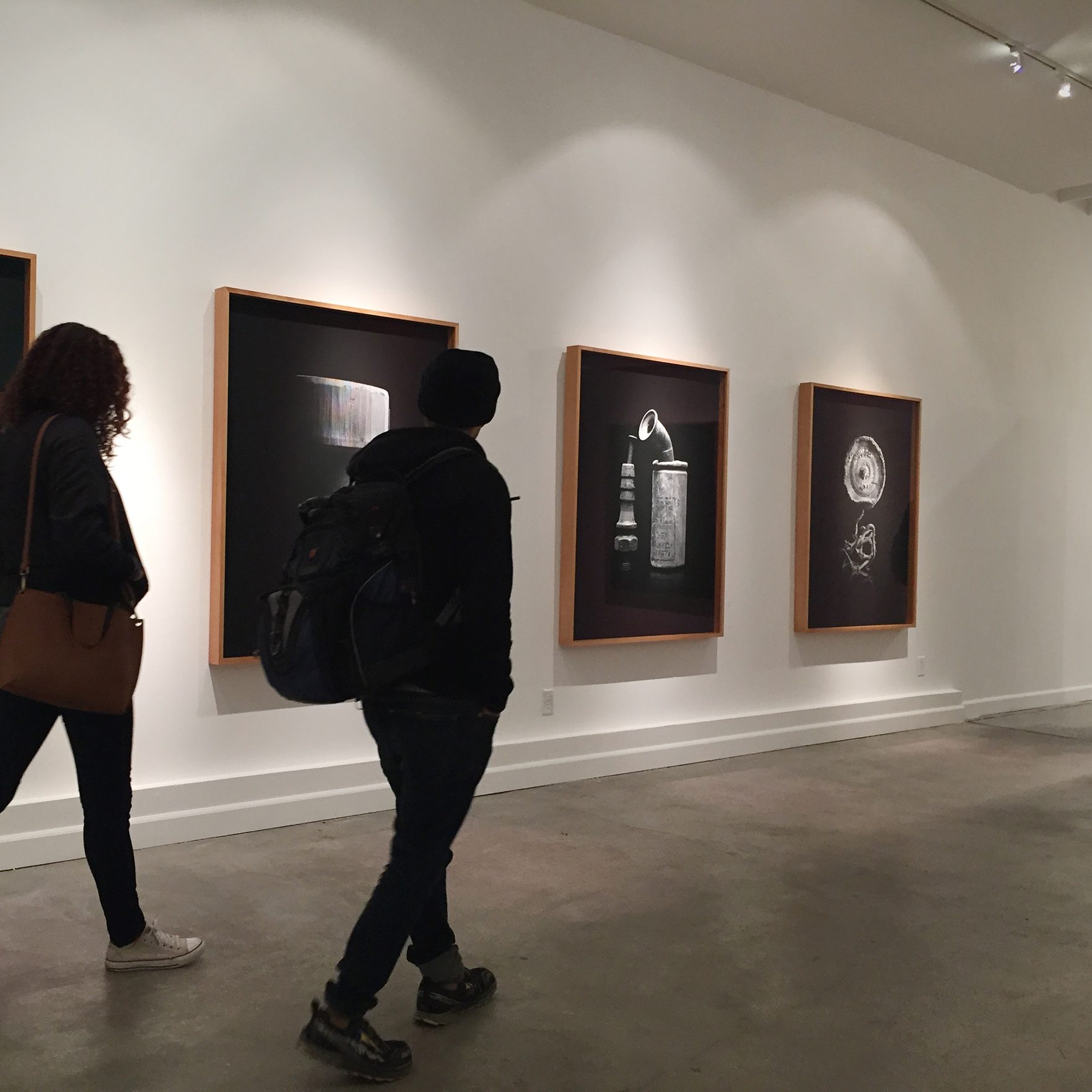 two figures walk in front of a series of black and white paintings.